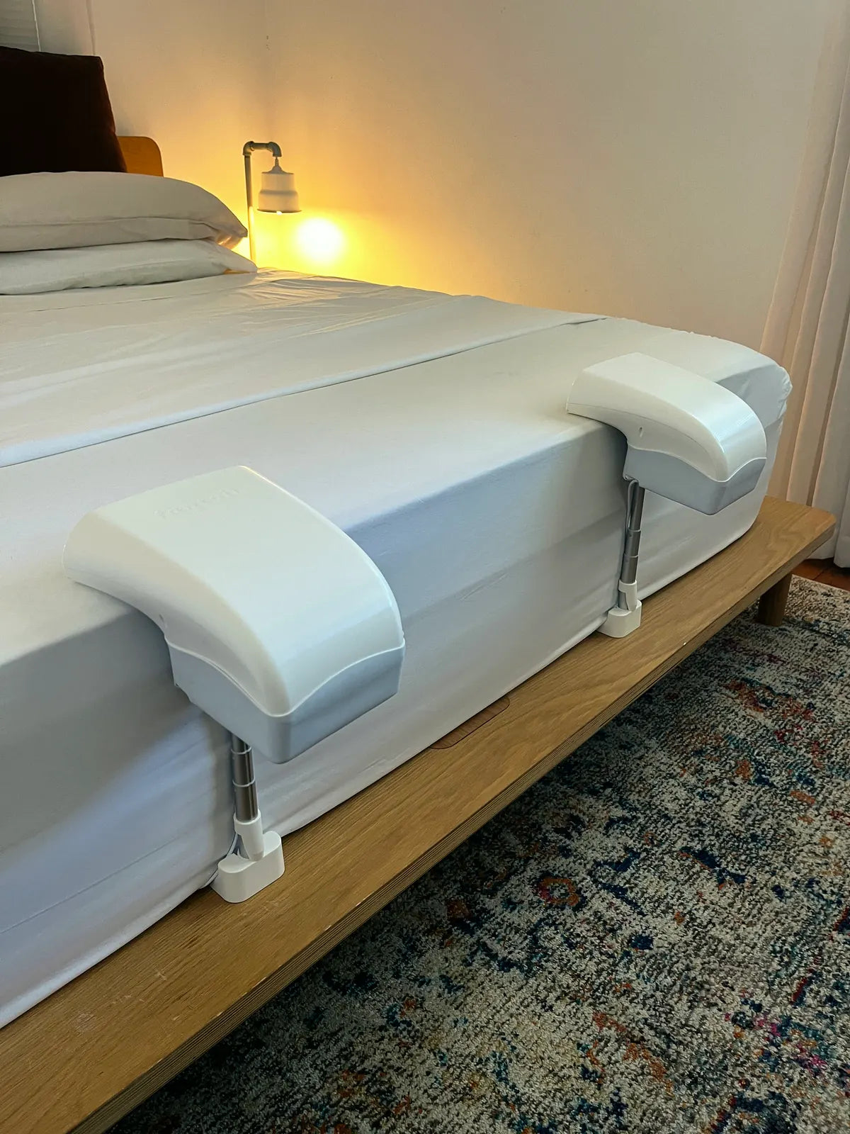 Two Fantail units clamped over the edge of a mattress, telescopic legs resting on the timber bed frame.